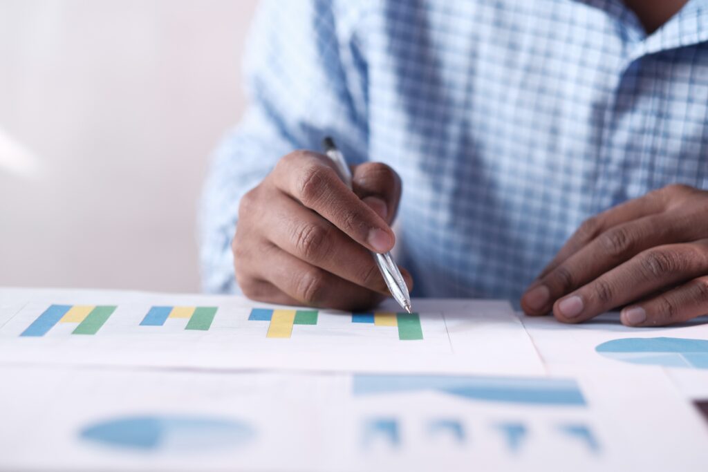 Close-up of professional hand pointing with pen at colorful bar graphs and pie charts evaluating case success rates for hiring workers compensation lawyer in Sherman Oaks California