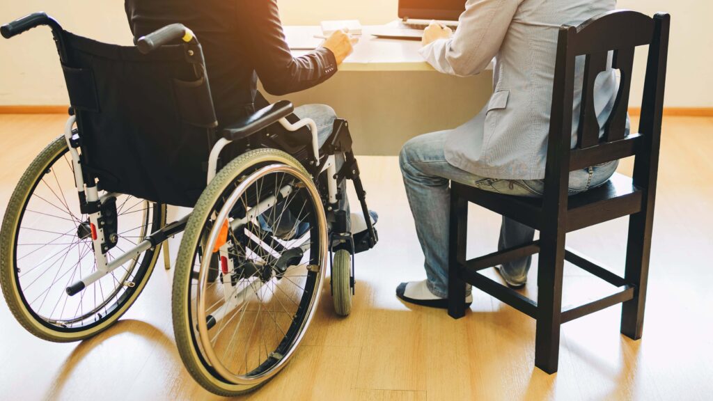 Person in wheelchair meeting with advisor at desk with laptop securing disability benefits and accommodations in Sherman Oaks California